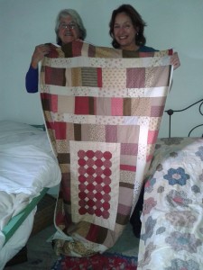 Norma & Irene holding up patchwork quilt.